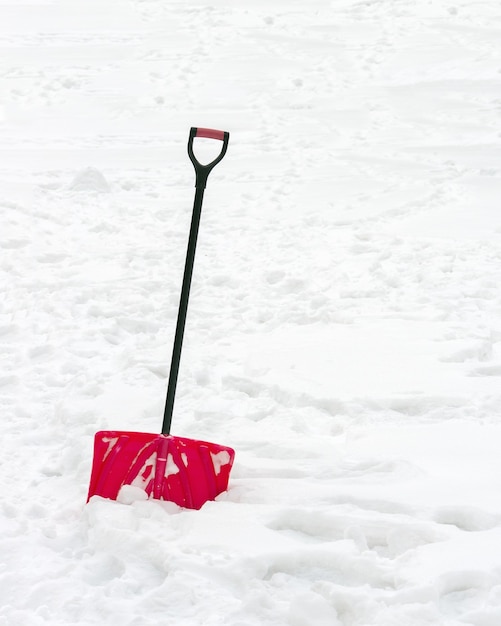 Rode plastic schop met zwart handvat geplakt in donzige witte sneeuw.