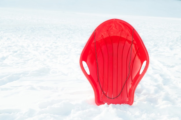 Foto rode plastic slee, slee, slee op witte besneeuwde achtergrond buitenshuis. winterspel en activiteit voor kinderen