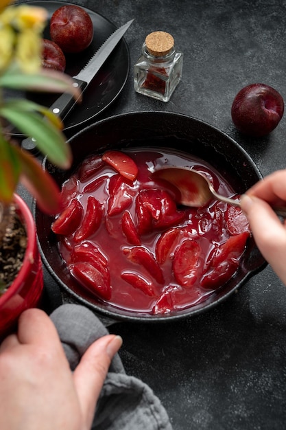 Rode pruimen confiture of jam Vrouwelijke handen fruitsaus mengen in zwarte koekenpan