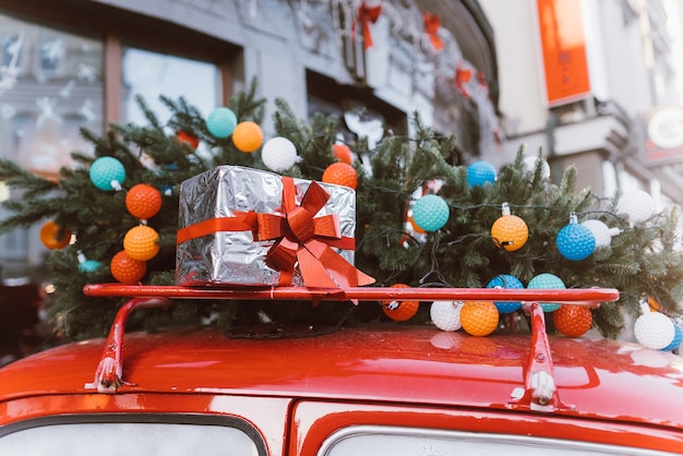 Rode retro auto met een kerstboomspar die aan het dak wordt gebonden, het symbool van de familiefeest.