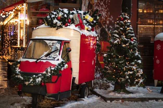 Rode retro bestelwagen versierd voor Kerstmis met een kerstboom op het dak en een dennenboom versierd met speelgoed