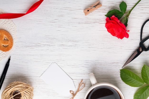 Rode roos, koffie, schaar en andere kleine voorwerpen op witte houten tafel, bovenaanzicht