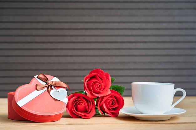 Rode rozen en geschenkdoos met koffiekopje op houten tafel