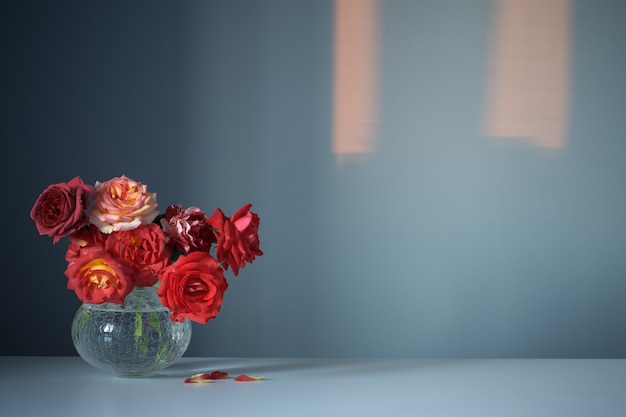 Rode rozen in glazen vaas op blauwe achtergrond