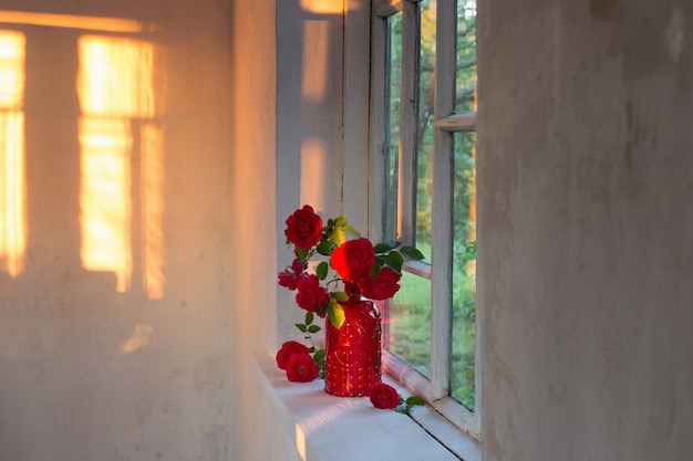 Rode rozen in rode glazen vaas op vensterbank