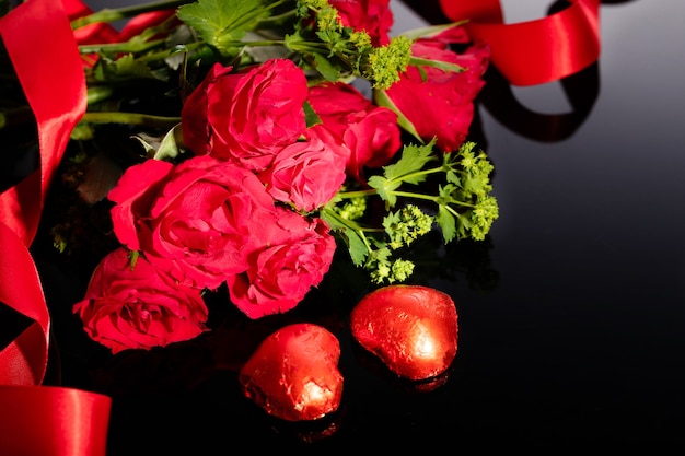 Rode rozenboeket en hartvormige chocolaatjes, rood lint op een zwarte achtergrond