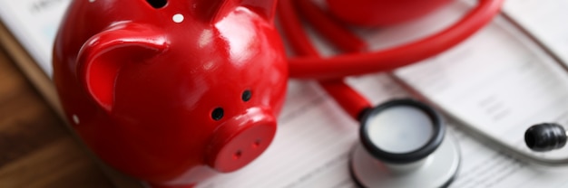 Rode spaarvarkenstethoscoop en stuk speelgoed hart die bij de vorm van de ziektekostenverzekeringseis liggen