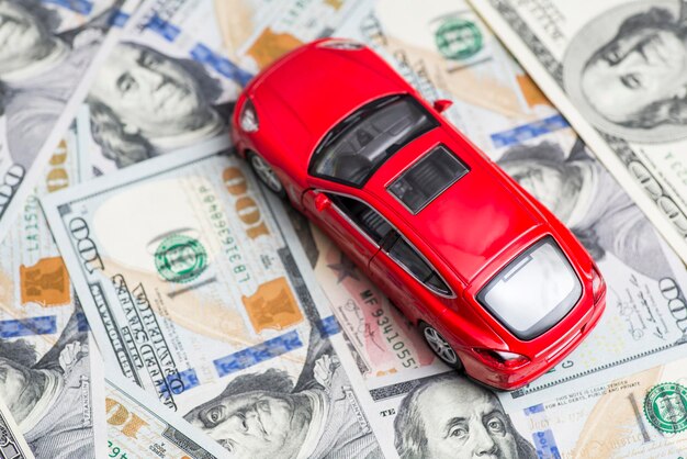 Rode speelgoed auto staat op dollar biljetten kosten van het kopen van een auto brandstof