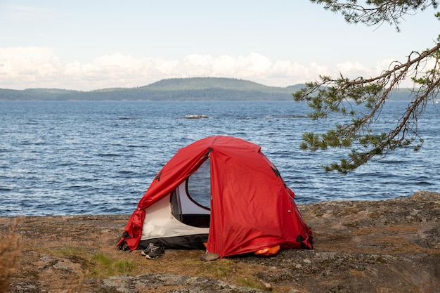 Rode tent met uitrusting op de rotsachtige oever van het meer