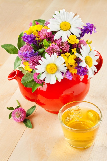 Rode theepot met boeket van geneeskrachtige kruiden en bloemen kopje gezonde thee op tafel kruidengeneeskunde