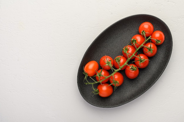 Rode tomaten op een groene tak op een donkere schotel op een houten achtergrond.