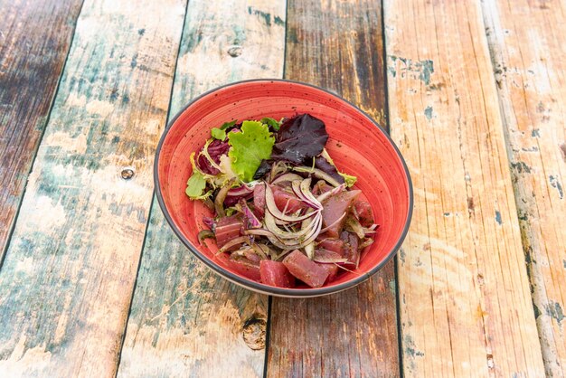 Rode tonijnceviche met gehakte rode ui en malse scheuten van diverse soorten sla in een rode kom