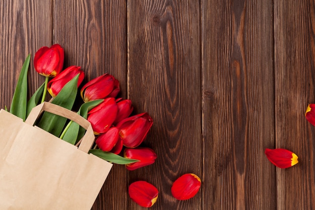 Rode tulpen boeket in papieren zak over houten tafel achtergrond met kopie ruimte