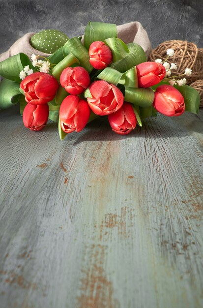 Rode tulpen, de lentedecoratie en geschilderde eieren op grijze rustieke achtergrond, tekstruimte