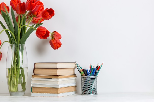 Rode tulpen in een vaas, boeken en schoolbenodigdheden op wit.