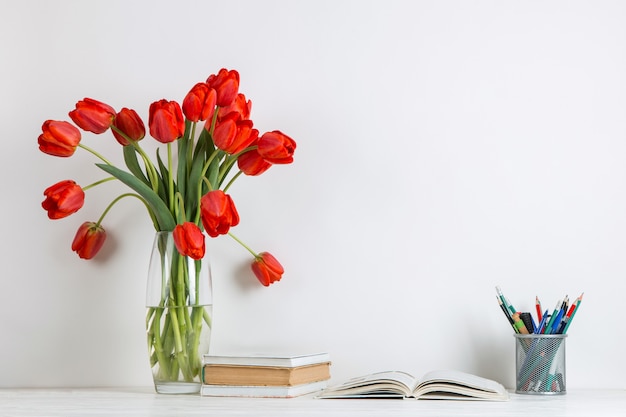 Rode tulpen in een vaas, boeken en schoolbenodigdheden op wit.