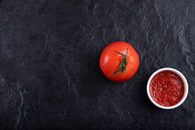 Rode verse tomaat met saus die op een zwarte achtergrond wordt geplaatst.