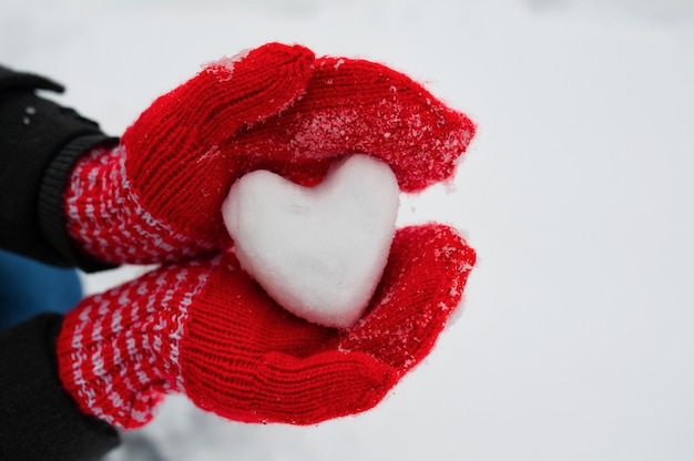 Rode vrouwelijke handschoenen houden een wit hart van de sneeuw