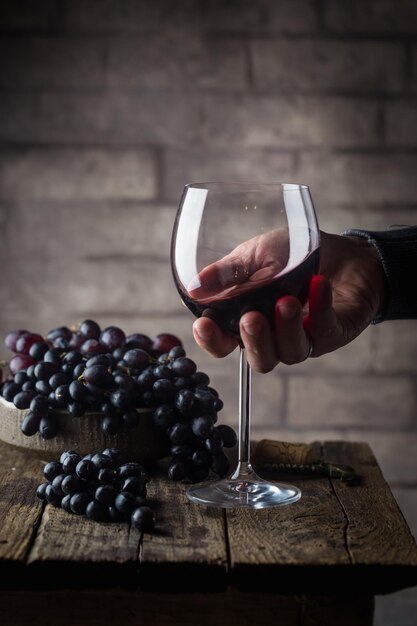 Rode wijnglas in een mannenhand en rijpe druiven op houten achtergrond