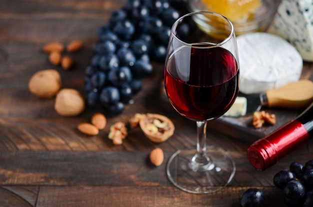 Rode wijnglas met kaas, druiven, honing en noten op een houten tafel