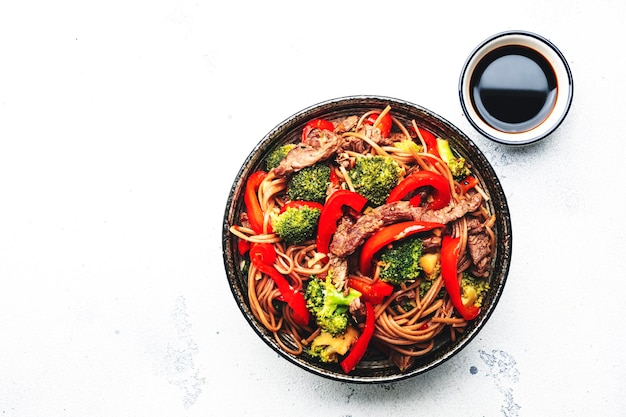 Roerbak noedels met groenten en rundvlees paprika en broccoli met sesamzaadjes in kom op witte tafel achtergrond bovenaanzicht