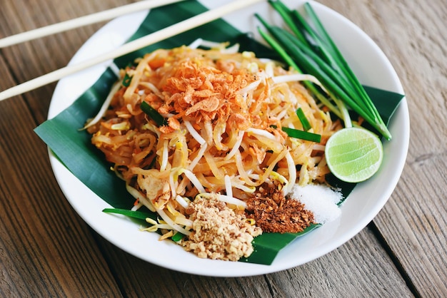 Roerbak noodle Pad Thai op bord geserveerd op de eettafel eten Thais eten gebakken noedel Thaise stijl met garnalen taugé en garnituur pinda's chili poeder suiker citroen limoen bovenaanzicht