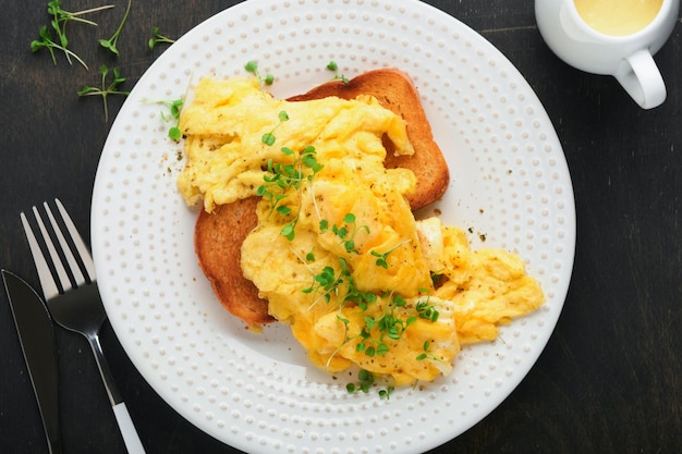 Roerei fluffy en buttery roerei op brood met microgreen radijs en hollandaise saus op witte plaat over donkere oude houten achtergrond zelfgemaakte ontbijt of brunch maaltijd bovenaanzicht