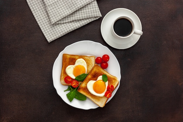 Roerei in de vorm van hart op plaat met tomaten, greens en koffie