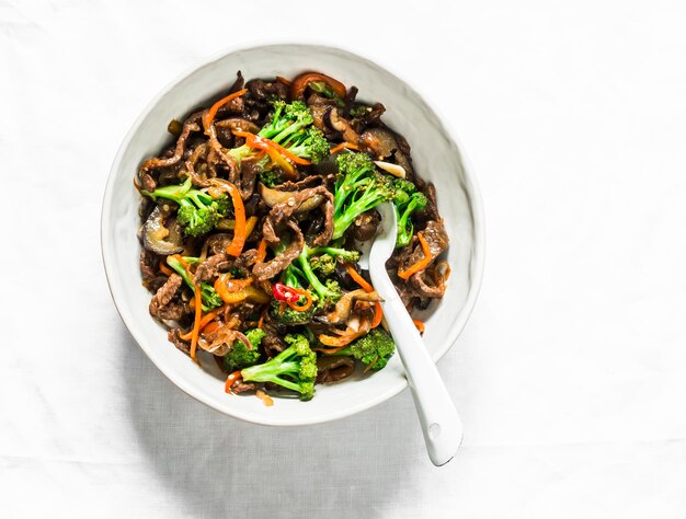 Roergebakken rundvlees met broccoli, wortelen en chilipepers op een lichte achtergrond bovenaanzicht