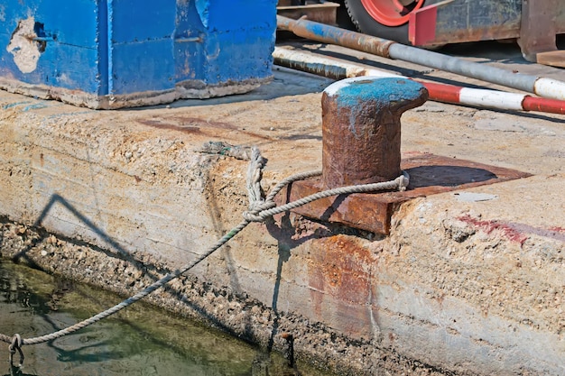 Roestige bolder met touw aan de kust