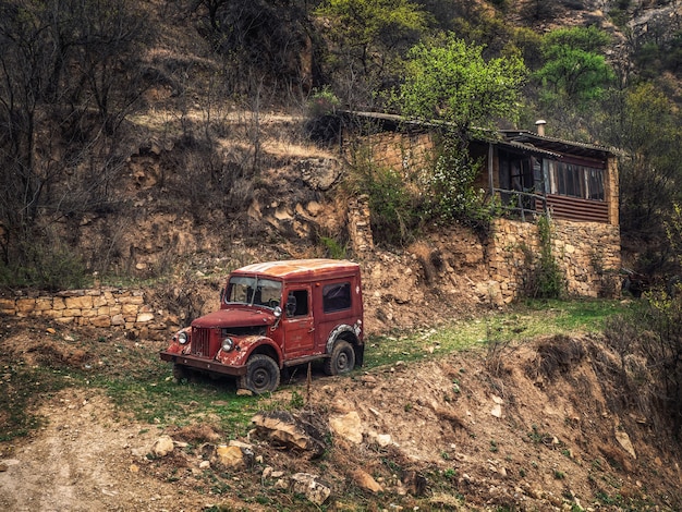 Roestige Gaz-69 auto op een helling bij een huis in een bergdorp. Dagestan. Rusland.