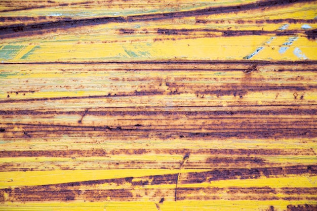 Roestige gele metaaloppervlakte met horizontale krassporen als achtergrond