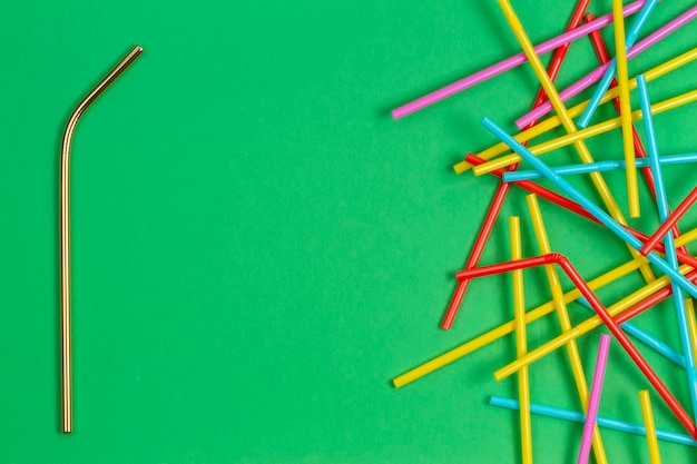 Roestvrijstalen herbruikbaar rietje met veel veelkleurige plastic rietjes op groene achtergrond