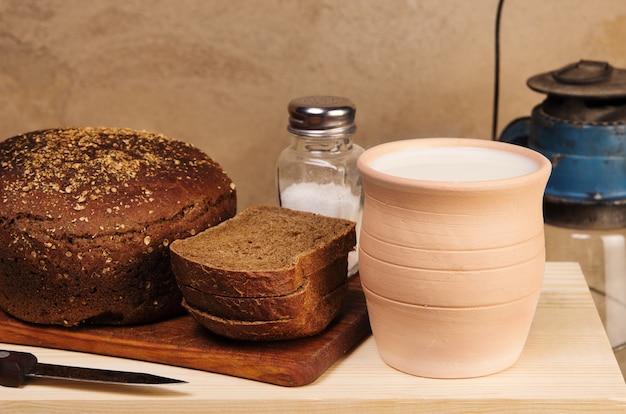 Roggebrood met zout op een snijplank aarden pot met melk en een petroleumlamp