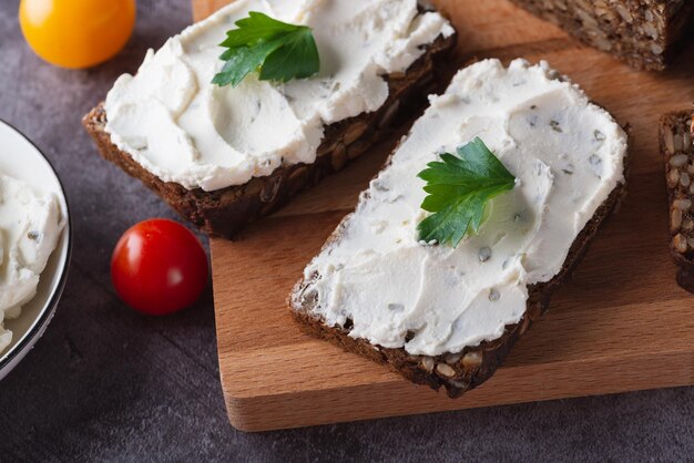 Roggebrood op een houten snijplank met kwark en ricotta en kruiden versierd met groene kruiden