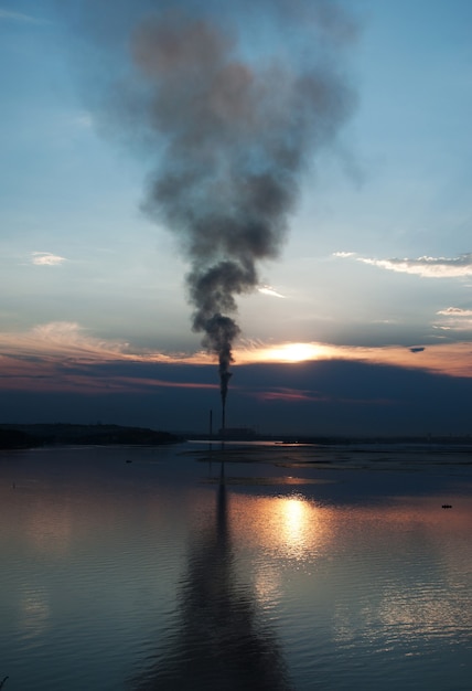 Rokende schoorstenen in de buurt van het meer in de avondlucht.