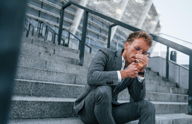 Rokende sigaret Jonge zakenman in grijze formele kleding is buiten in de stad