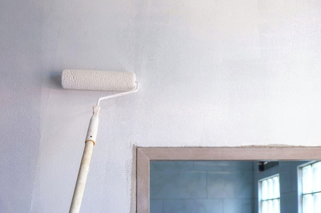 Rolborstel met lange steel die witte grondverf aanbrengt op betonnen muur in huisbouwplaats