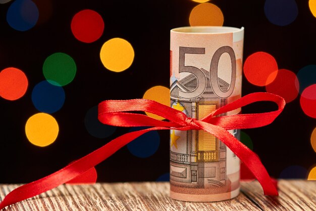 roll of 50 euro bills with ribbon against of colorful lights