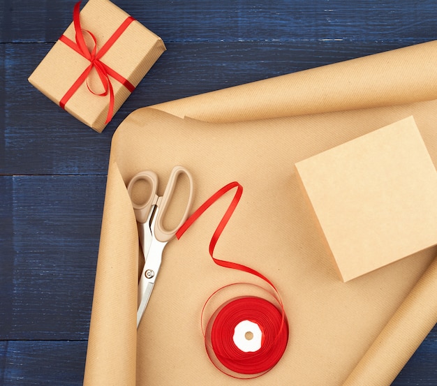 Roll of brown kraft packaging paper, box tied with a red silk ribbon, scissors