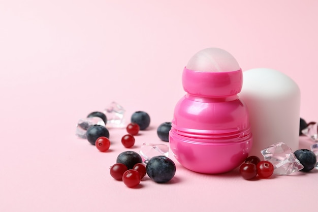 Roll-on deodorant, ice cubes and berries on pink background