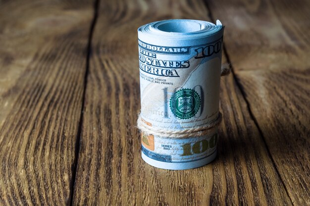 A roll of dollars stands on a wooden textured table.