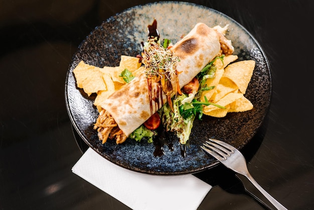 Roll filled with pulled pork meat with green salad and chips on dark background