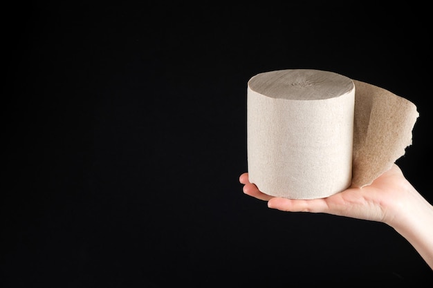 A roll of grey recycled toilet paper on a black background with space for text