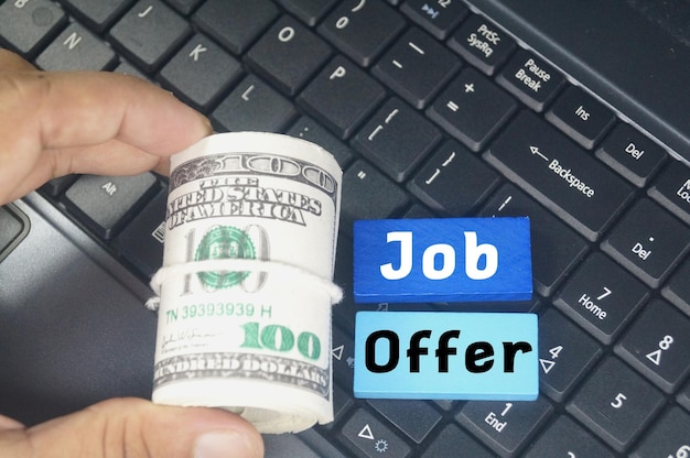 A roll of money is on top of a keyboard with the words job offer on it.