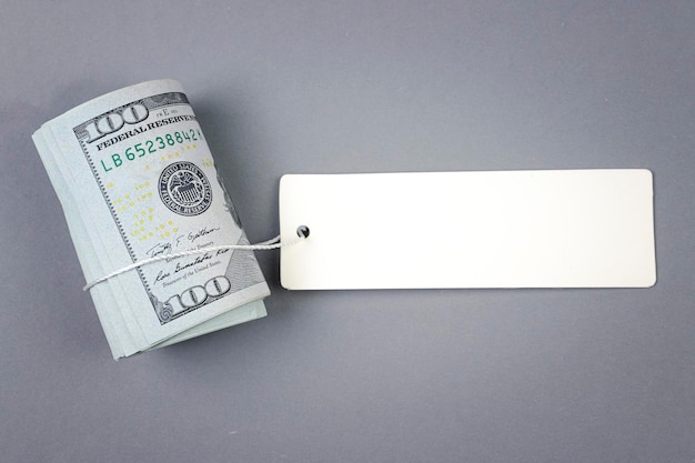 Roll of money with blank white cardboard price tag or label One hundred American dollars viewed from above with copy space