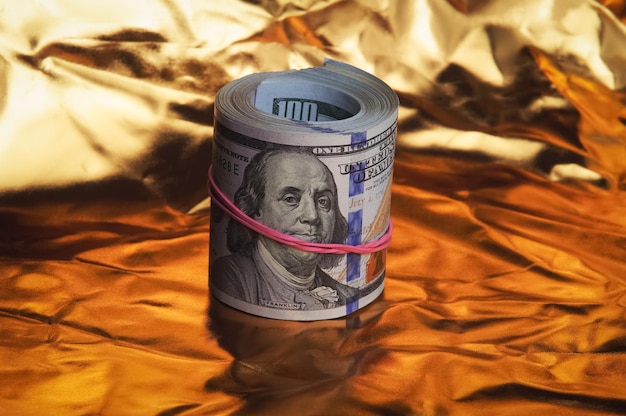 Photo a roll of one hundred american dollars in closeup on a gold background a big pile of cash dollars