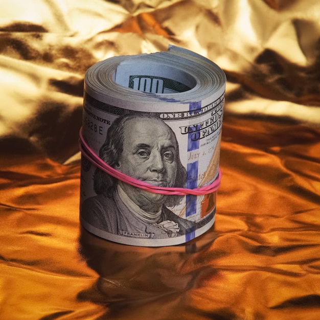 Foto un rotolo di cento dollari americani in primo piano su fondo oro un grosso mucchio di dollari in contanti