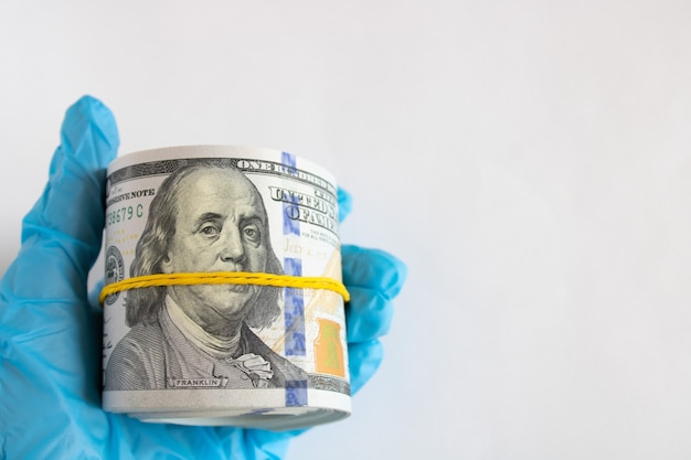 Roll of one hundred dollar bills in hand in medical glove on white background