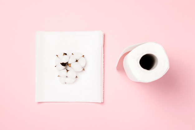 Roll of paper towels and cotton flowers on a pink background. Concept is 100% natural product, delicate and soft. Flat lay, top view